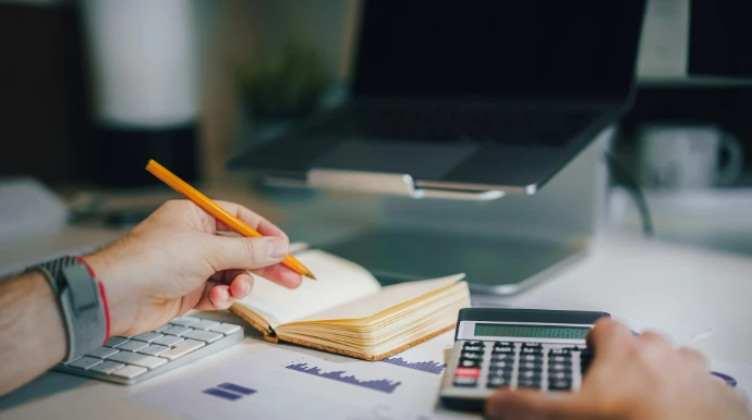 a person sitting at a desk with a calculator and a notebook